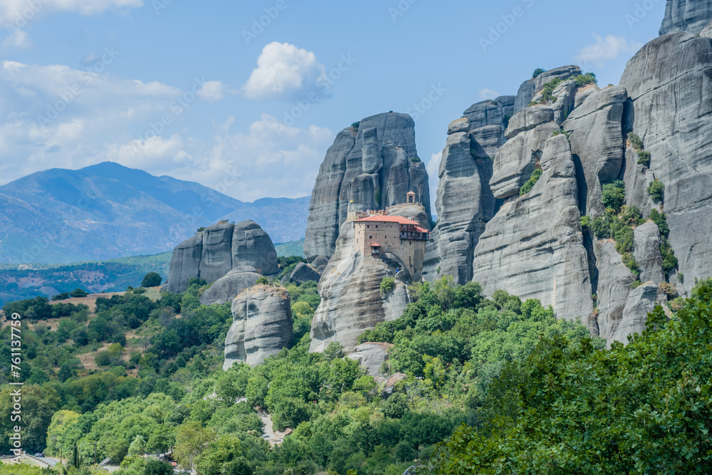 A panoramic view of monastery set against a backdrop of rugged cliffs and vegetation, in Meteora, Greece