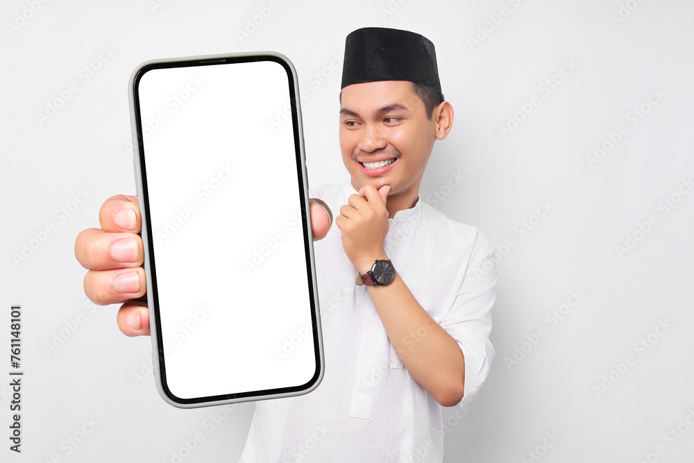 Smiling young Asian Muslim man showing smartphone screen, touching his chin, thinking about the offer on white background. People religious Islam lifestyle concept. celebration Ramadan and ied Mubarak Smiling young Asian Muslim man showing smartphone screen, touching his chin, thinking about the offer on white background. People religious Islam lifestyle concept. celebration Ramadan and ied Mubarak