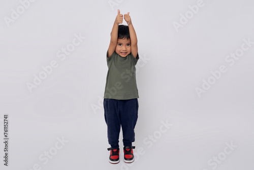 Full body little small smiling happy Asian boy 2-3 years old wearing green t-shirt standing confident while showing thumbs up like gesture isolated on white background