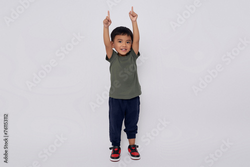 Full body little small smiling happy Asian boy 2-3 years old wearing green t-shirt standing confident while doing winner gesture isolated on white background