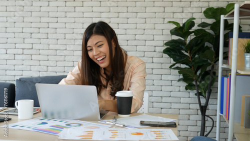 Asian Female freelance using laptop at home office desk. Woman reading financial graph chart Planning analyzing marketing data. Asian female people working office firm with business stuff, coffee cup photo