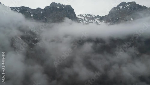Misty clouds hang low as epic ridgeline rocks of alpine mountains with snow jut into sky