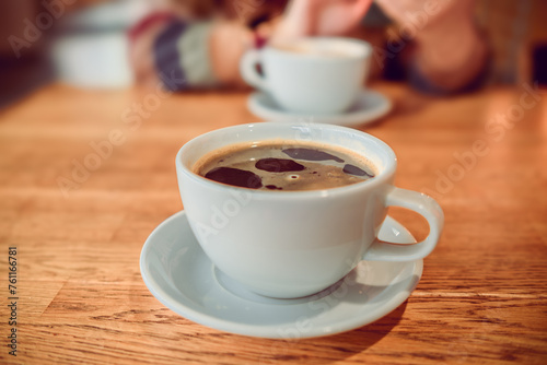 Two cups of coffee resting on a wooden table, representing a cozy coffee break moment in a comfortable setting.