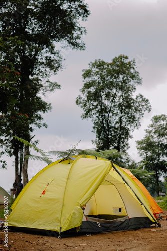 A yellow tent like lemon lime stood firmly on the camping site against a backdrop of trees and a slightly cloudy sky, along with an orange tent behind it