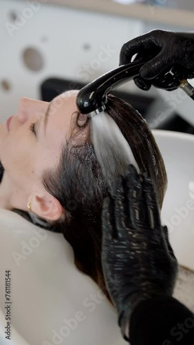 Professional hairdresser washing hair of a beautiful young woman in hair salon.
