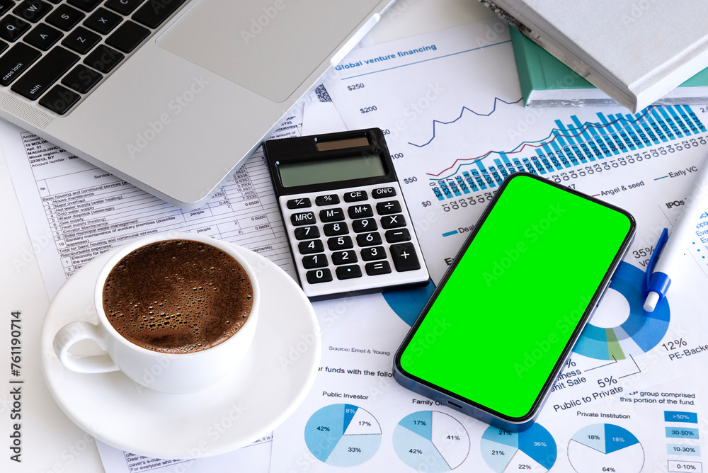 Smartphone with chroma key green screen, calculator, diagrams and graphics on paper, cup of coffee on office workplace.Wealth and investment concept. Smartphone with chroma key green screen, calculator, diagrams and graphics on paper, cup of coffee on office workplace.Wealth and investment concept.