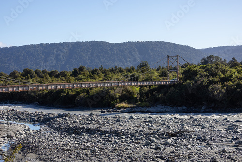Bücke über einem Flussbett in Neuseeland mit Hubschrauber am Himmel 