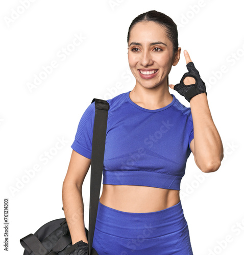 Athletic Caucasian young woman with gym bag on studio background showing a mobile phone call gesture with fingers.