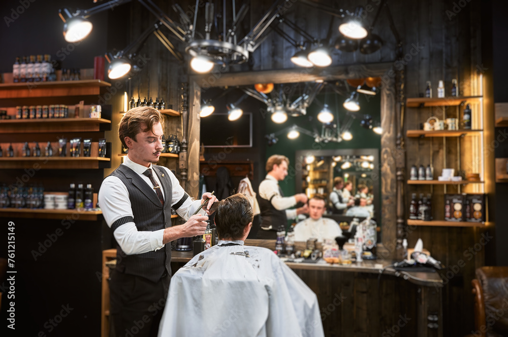Cropped photo of handsome hairdresser in fancy outfit cutting wet hair. Young customer getting fresh hairstyle from professional barber. Back view of male getting haircut.