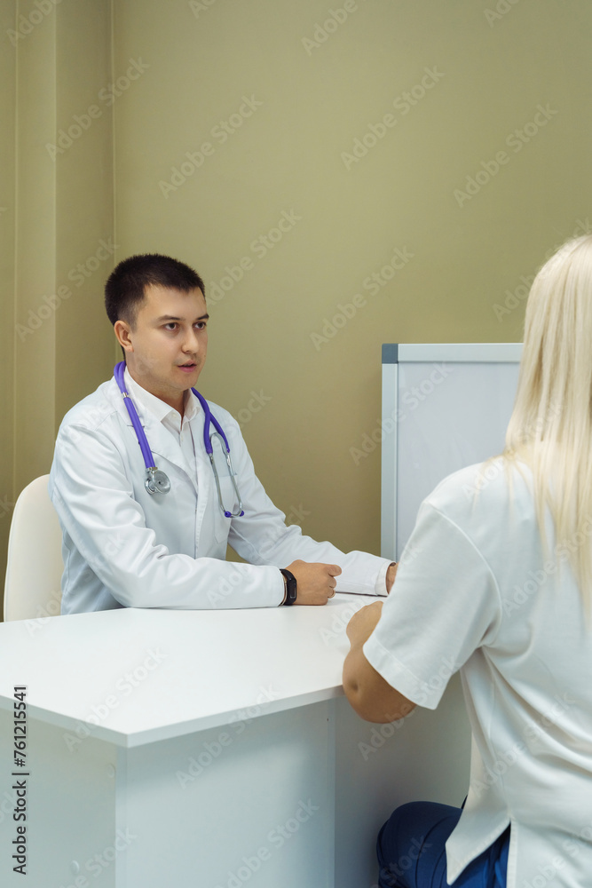 Fototapeta premium Doctor consulting Patient. Professional physician wearing white coat talking to woman at appointment visit in clinic.