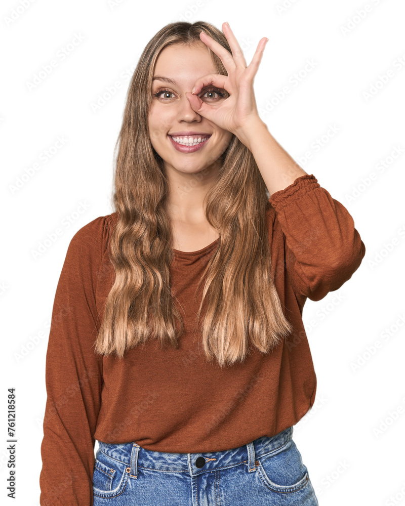 Studio portrait of a blonde Caucasian woman excited keeping ok gesture on eye.
