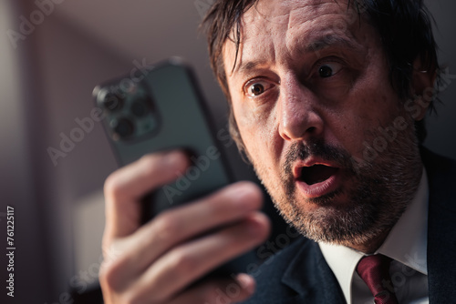 Shocked businessman reading text message on smartphone with surprised facial expression