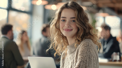 A smiling woman with a laptop in a sunlit office space.