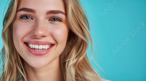 Photo with space for text. Portrait of a blonde girl with a smile and white teeth on a blue matte background. Suitable for advertising © Olga Troitskaja