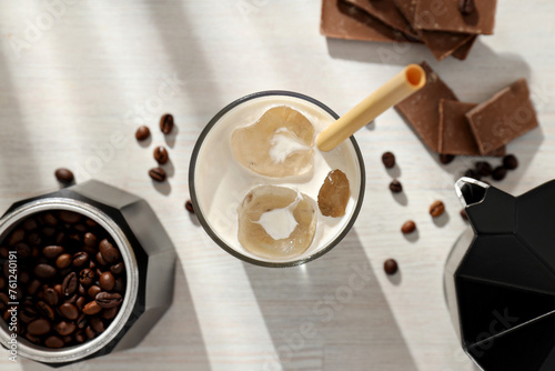 Glass with iced coffee, coffee maker with coffee bean and pieces of chocolate on light background, top view