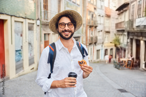 Smiling young man holding coffee cup and traditional dessert pastel de nata photo