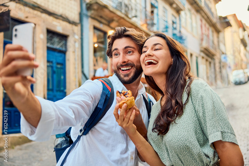 Cheerful couple holding traditional dessert pastel de nata and taking selfie through smart phone photo