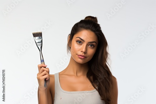 Young woman artist holding a large paintbrush, with a confident expression, against a white background