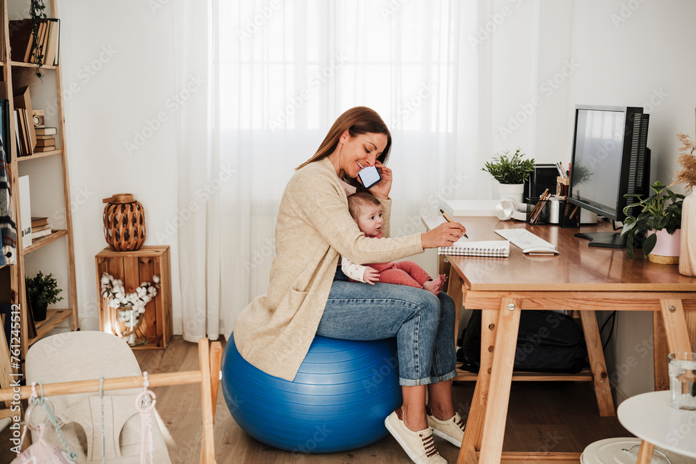 Mother sitting with baby girl and talking on mobile phone in home office Mother sitting with baby girl and talking on mobile phone in home office