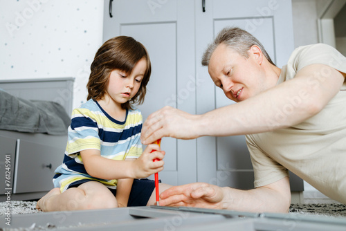 Son assembling nightstand using screwdriver with father at home photo