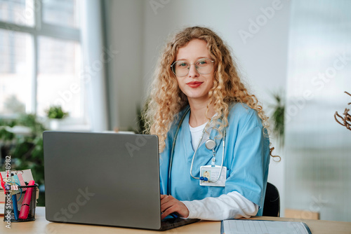 Smiling doctor sitting near laptop in hospital photo