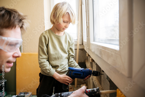 Boy drilling wall near father using caulk gun at home