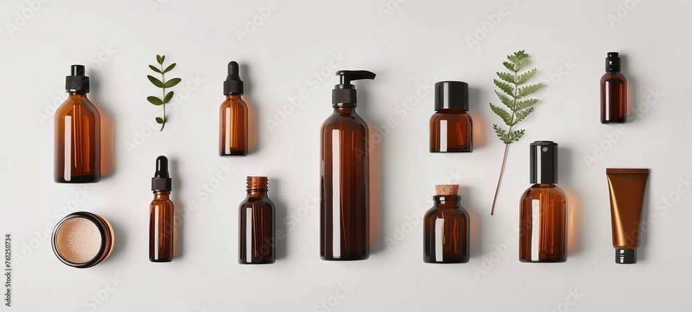 Cosmetic packaging. Set of various amber glass bottles and containers for skincare products, neatly arranged with green botanical elements on a clean white background.