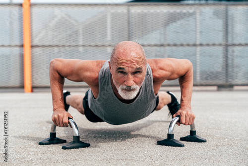 Determined senior man doing plank exercise on handles photo