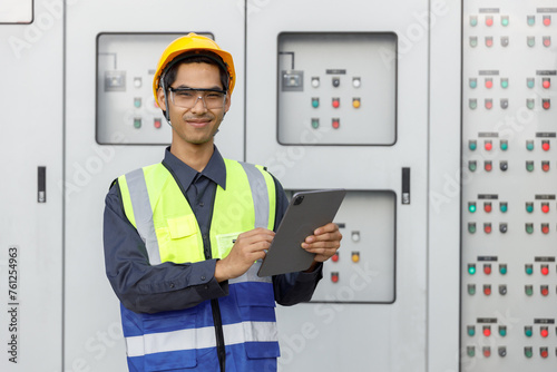 Electrical engineer man using tablet checks switchboard main Distribution Boards control panel electric factory building. Male Industrial technician worker working power distribution room.