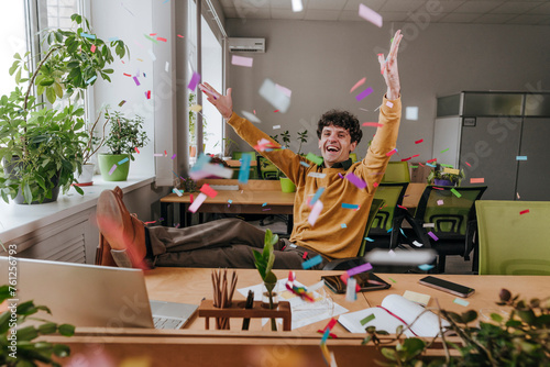Carefree businessman throwing confetti at desk in office photo