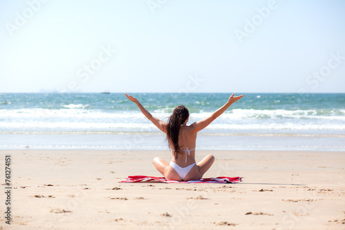 A beautiful girl with a wet hair and an Asian face type, a good slender figure posing on a sandy beach against the background of the ocean. Woman dressed white bikini and red striped towel