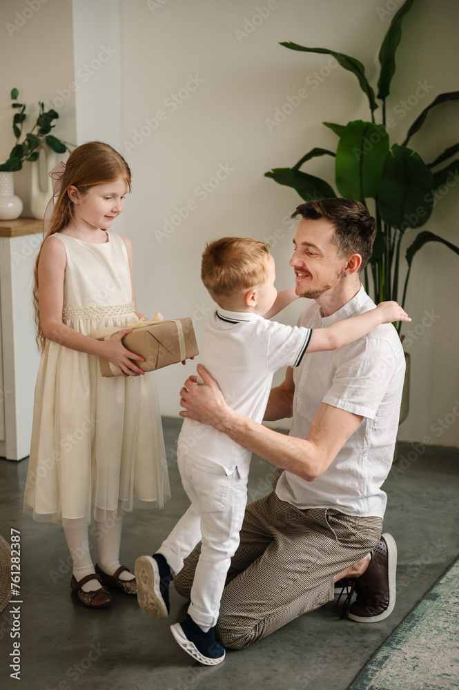 Fototapeta premium Son hugging and greeting father. Daughter gives present box gift smiling dad. Child makes surprise for Fathers Day. Children congratulate daddy in kitchen. International Mens Day. Happy family holiday