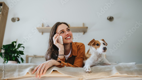 Fotografie Beautiful single woman lying on bed, petting her dog, and making phone call