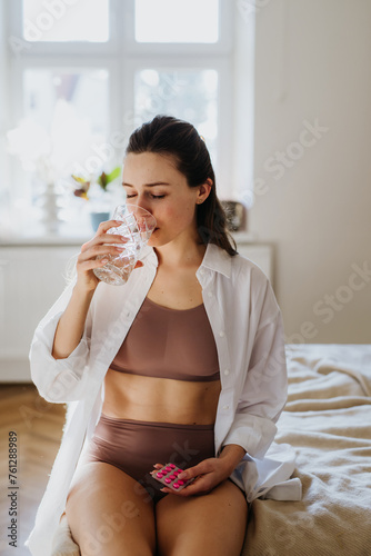 Woman taking pills with water, suffering from menstrual pain, having cramps. Close up of woman holding abdomen, endometriosis, and conditions causing pain in tummy. photo