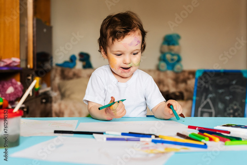 a small boy draws with colorful markers on a piece of paper