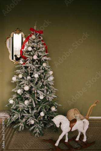 Beautiful New Year decor, a Christmas tree on the background of an olive wall and a horse made of wood