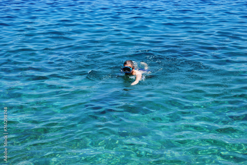 Horizontal photo of man swiming with mask and exploring Adriatic sea bottom. Young man swiming in a diving mask