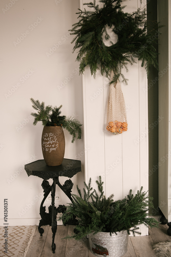 Beautiful New Year decor, a Christmas wreath made of spruce on the wall, a handmade woven string bag with tangerines