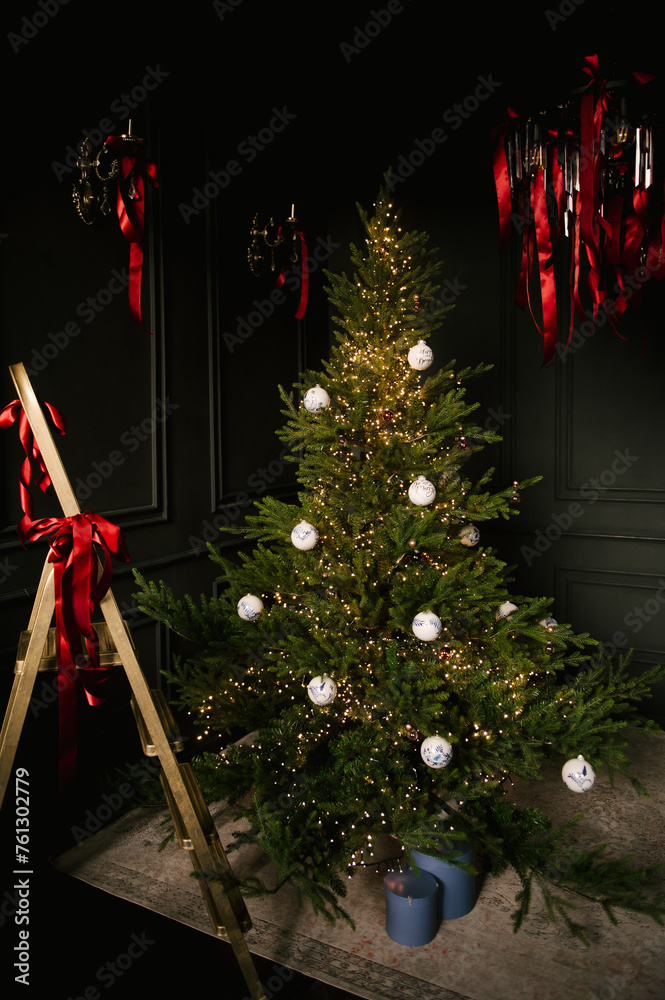 Beautiful New Year decor, a Christmas tree with a golden staircase in the stylish dark interior of the living room