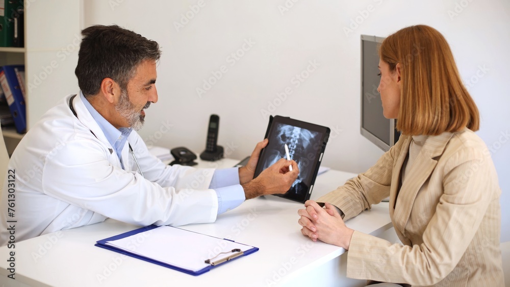 Doctor consulting patient with spine X-ray on tablet in a medical office setting Doctor consulting patient with spine X-ray on tablet in a medical office setting