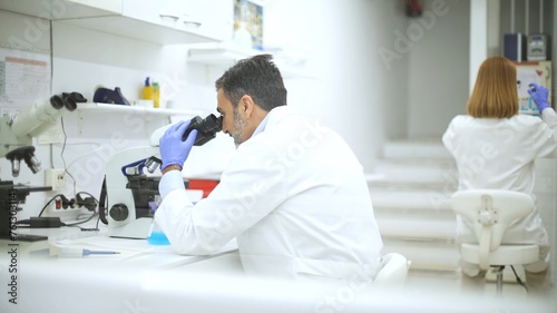 Male and female scientists working separately on microscopes in a laboratory