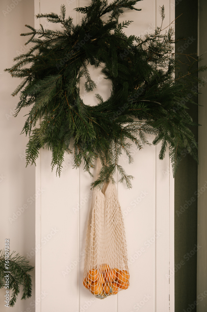 Beautiful New Year decor, a Christmas wreath made of spruce on the wall, a handmade woven string bag with tangerines