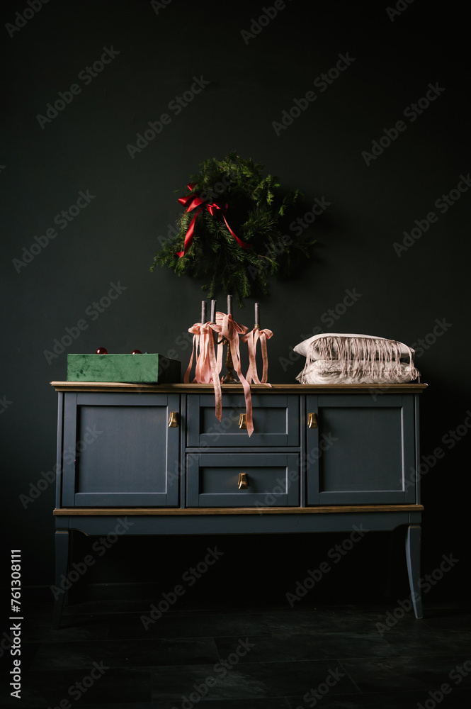 Beautiful New Year decor, a Christmas wreath on a vintage chest of drawers in a stylish dark living room interior
