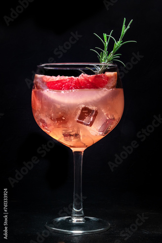 Cocktail with fresh fruit. Gin and tonic drink with ice at a party, on a black background. Alcohol with pink graperfuit and rosemary