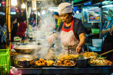 Thai woman cooking fried noodle on street food market.