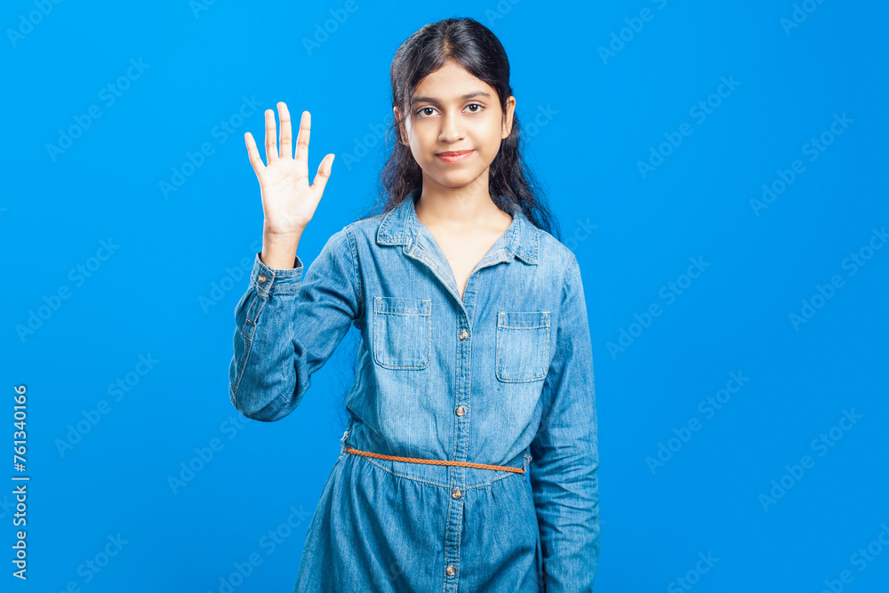 young Indian girl saying hello greeting, showing wave hand on blue background young Indian girl saying hello greeting, showing wave hand on blue background