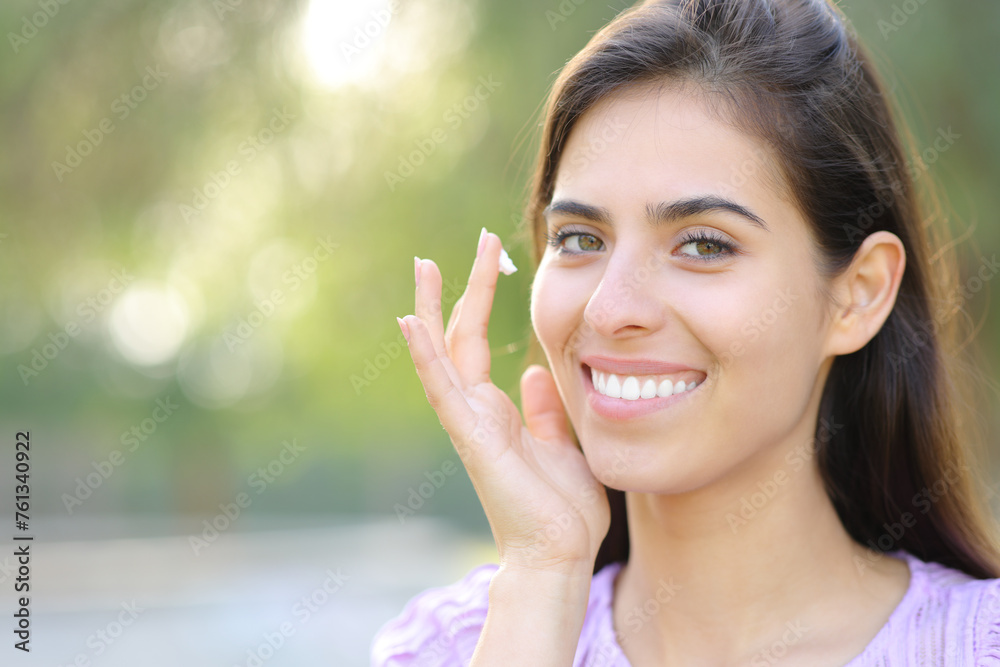 Happy woman applying moisturizer looking at you Happy woman applying moisturizer looking at you