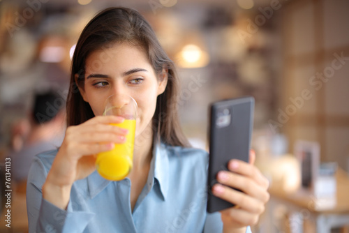 Woman drinking orange juice checking phone in a bar