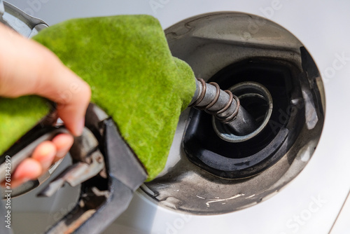Close up image of hand refilling a car with fuel at a gas station, green fuel nozzle, energy concept