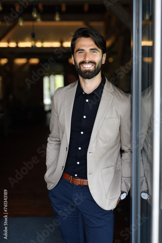 Portrait of mature businessman in suit jacket standing indoors in modern office. photo